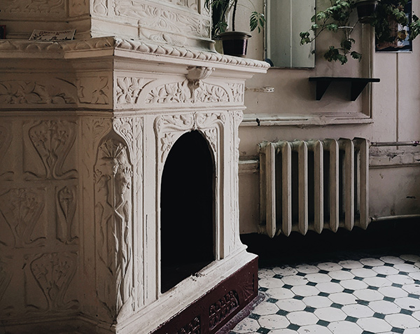 Mantoloking boiler repair helps keep old radiators like the white one pictured working well. Also shown is ornate white fireplace and a house plant hanging in the corner.