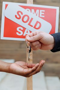 Homes for sale in Tinton Falls SOLD sign in back of hands passing a set of keys