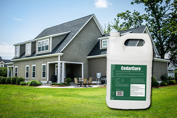 CedarCure bottle over a green sided house with a lush healthy lawn